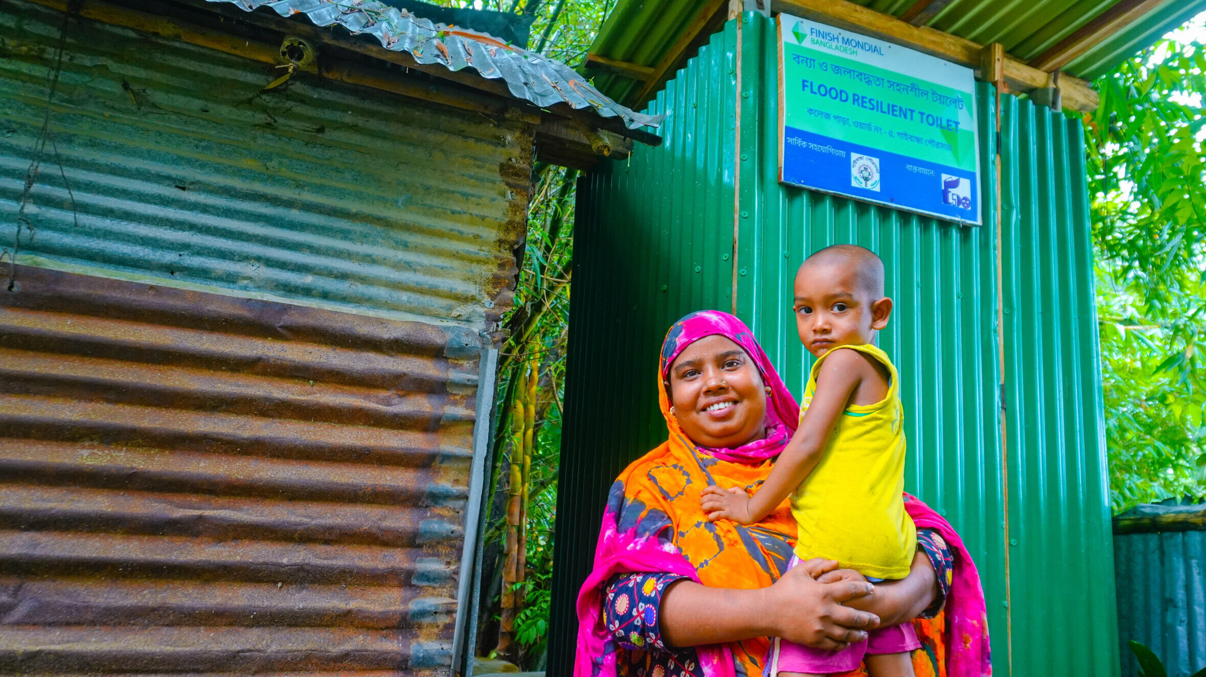 Woman holding her child and smiling in front of a flood resilient toilet